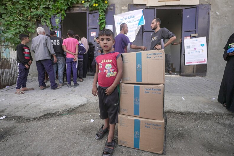 A child standing next to WFP food parcels in Gaza.