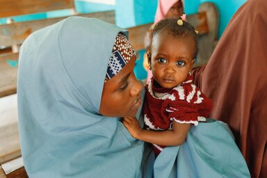 一位母亲和她的孩子在保健中心门口，她的孩子被诊断出患有严重急性营养不良 (SAM)，这是她第一次探望孩子。