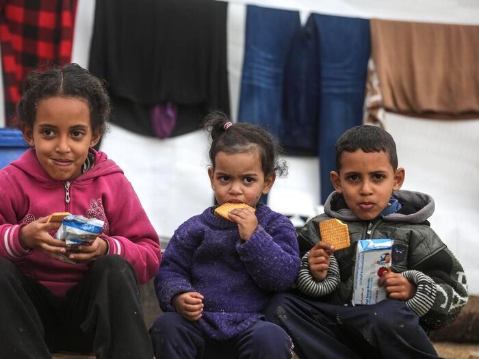 Three children sat and eating WFP biscuits.