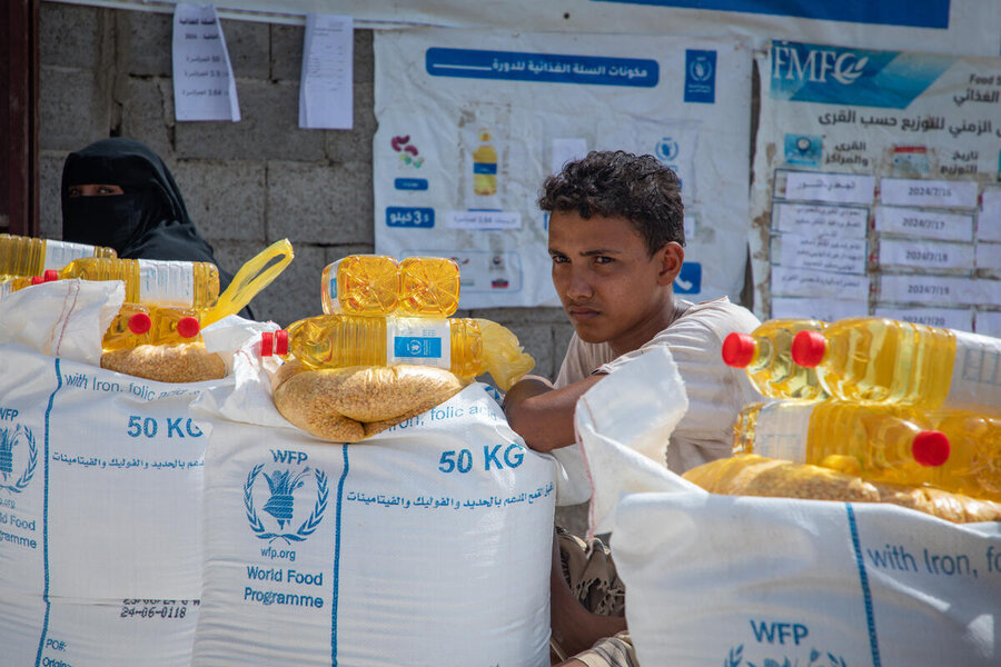 A boy is sat in front of several sacks of WFP food.