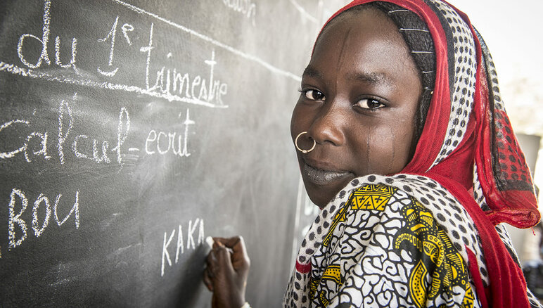 Kaka Marabou在乍得湖旁的一所学校的黑板上写下她的名字。 乍得湖流域的难民、流离失所者和贫困社区的人们依赖人道主义援助生存，接受基础教育的机会非常有限。 照片 © WFP/Giulio d'Adamo